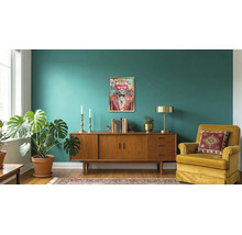 Modern eingerichteter Wohnraum mit einem Sideboard aus Holz, einem Wandbild eines Leoparden mit Brille, einem Polstersessel, einer Zimmerpflanze und einem Teppich.