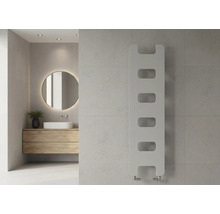 Moderner vertikaler Design-Heizkörper mit Aussparungen an einer Fliesenwand im hellen Badezimmer mit Holzwaschtisch und rundem Spiegel.