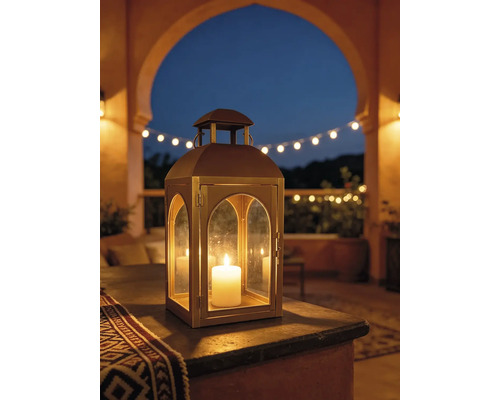 Metalllaterne mit Rundbogen-Glasfenstern und brennender Kerze auf einer Terrasse bei Dämmerung, mit Lichterkette im Hintergrund.