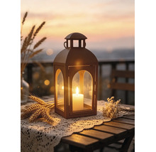 Laterne mit brennender Kerze auf einem Holztisch mit Spitzendeckchen, Weizen und Trockenblumen vor einem stimmungsvollen Sonnenuntergang.