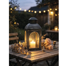 Metalllaterne mit brennender Stumpenkerze auf einem Holztisch im Garten, dekoriert mit Trockenblumen und Blättern.