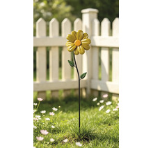 Gartenstecker aus Metall in Form einer gelben Blume mit orangefarbener Mitte in einem Garten mit weißem Lattenzaun.
