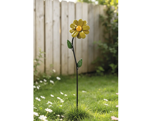 Helle Außenszene mit einem dekorativen Gartenstecker aus Metall in Form einer Blume mit Blättern, der in einem Rasen vor einem Zaun steht.