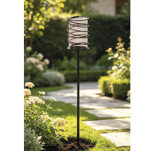 Moderne Gartenfackel mit schwarzem Erdspieß und spiralförmigem Gehäuse in einer hellen, gepflegten Gartenlandschaft.