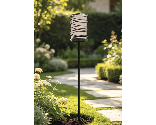 Moderne Gartenfackel mit schwarzem Erdspieß und spiralförmigem Gehäuse in einer hellen, gepflegten Gartenlandschaft.