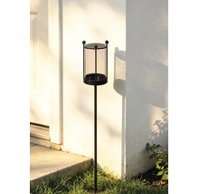 Gartenfackel mit Glaseinsatz und schwarzem Metallgestell auf einem Erdspieß vor einer weißen Hauswand.