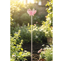 Pinker Gartenstecker in Schmetterlingsform, aufrecht platziert in der Erde eines hellen Gartens zwischen Pflanzen und weißen Blumen.