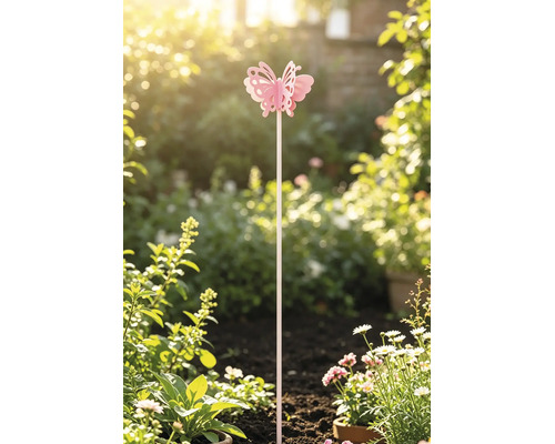 Pinker Gartenstecker in Schmetterlingsform, aufrecht platziert in der Erde eines hellen Gartens zwischen Pflanzen und weißen Blumen.