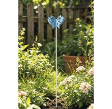 Dekorativer Gartenstecker mit blauem Schmetterling in einem sonnigen Beet mit blühenden Blumen vor einem Holzzaun.