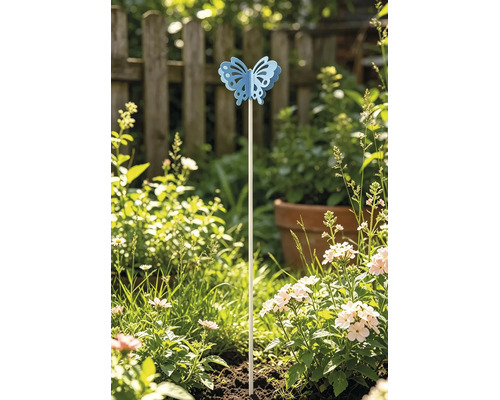 Dekorativer Gartenstecker mit blauem Schmetterling in einem sonnigen Beet mit blühenden Blumen vor einem Holzzaun.