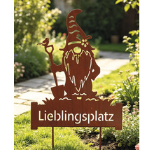 Rostiger Gartenstecker in Form eines Wichtels mit Schaufel und dem Schriftzug Lieblingsplatz, stehend in einem bepflanzten Garten.