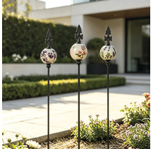 Drei Gartenstecker mit floral verzierten Keramikkugeln und Metallspitzen in einer modernen Gartenanlage mit gepflastertem Weg.