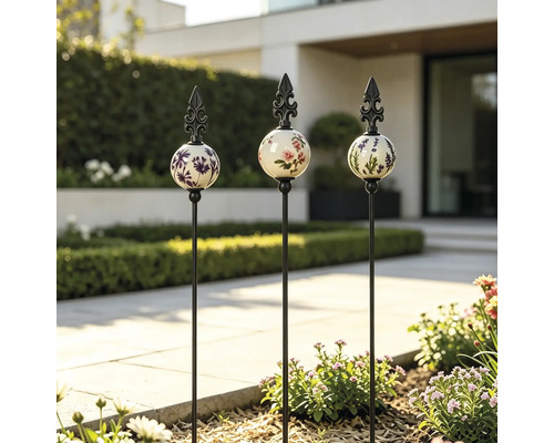 Drei Gartenstecker mit floral verzierten Keramikkugeln und Metallspitzen in einer modernen Gartenanlage mit gepflastertem Weg.