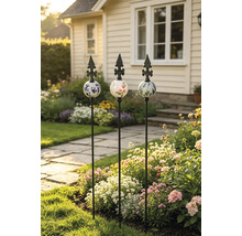 Drei dekorative Gartenstäbe aus Metall mit verzierten Keramikkugeln und Lilien-Spitzen in einem blühenden Gartenbeet.
