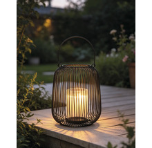 Schwarze Metalldrahtlaterne mit Glaseinsatz und brennender Kerze auf einer Holzterrasse im Garten.