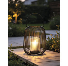 Modernes Windlicht aus schwarzem Metalldraht mit Glaseinsatz und leuchtender Kerze auf einer Gartenplatte.