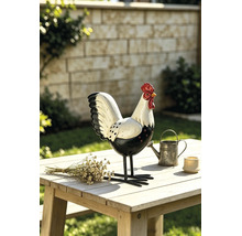 Dekorative Gartenfigur Hahn aus Metall auf einem hellen Holztisch im Garten neben einer kleinen Gießkanne und Trockenblumen.