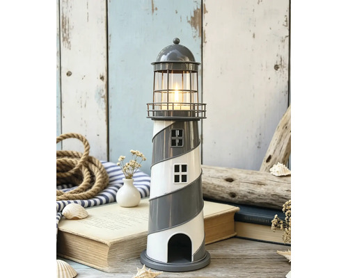 Dekorativer Teelichthalter als Leuchtturm mit Spiralmuster und brennender Kerze in einer maritimen Szene mit Seil, Büchern und Muscheln.