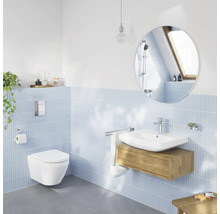 Helles, modernes Badezimmer mit wandhängendem WC, weißem Waschtisch auf Holzunterschrank, rundem Spiegel und hellblauen Wandfliesen.