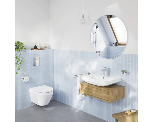 Helles, modernes Badezimmer mit hellblauen Wandfliesen, wandhängendem WC, Waschtisch mit Holzunterschrank und einem runden Spiegel.