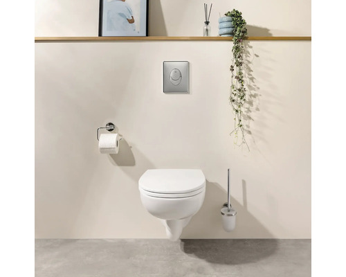 Wand-WC mit geschlossenem Deckel, Betätigungsplatte, Toilettenpapierhalter und WC-Bürste in modernem Badezimmer.
