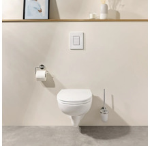 Modernes Wand-WC mit geschlossenem Deckel, Drückerplatte, Toilettenpapierhalter und Klobürste in einem minimalistischen Badezimmer.