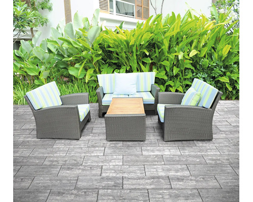 Terrasse mit grauen rechteckigen Steinplatten, einer Polyrattan-Gartenlounge und einem Holztisch vor grüner Bepflanzung.