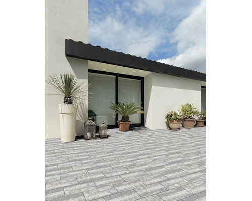 Helle, organisierte Terrasse mit modernen, grauen Pflastersteinen in Rechteckform, dekoriert mit Pflanzgefäßen und Laternen an einer weißen Fassade.