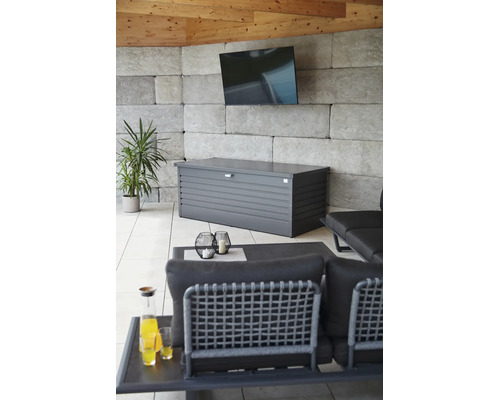 Gartenbox aus Metall in Anthrazit in modernem Loungebereich mit Steinwand, Fernseher und Gartenmöbeln.