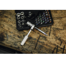 Steckschlüsselsatz und Bit-Satz in einem Kunststoffkoffer auf einer Werkbank aus Holz, mit einer kleinen Ratsche und einem Torx-Bit im Vordergrund.
