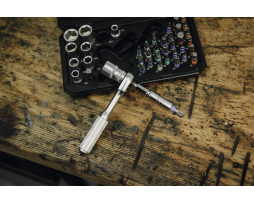 Steckschlüsselsatz und Bit-Satz in einem Kunststoffkoffer auf einer Werkbank aus Holz, mit einer kleinen Ratsche und einem Torx-Bit im Vordergrund.