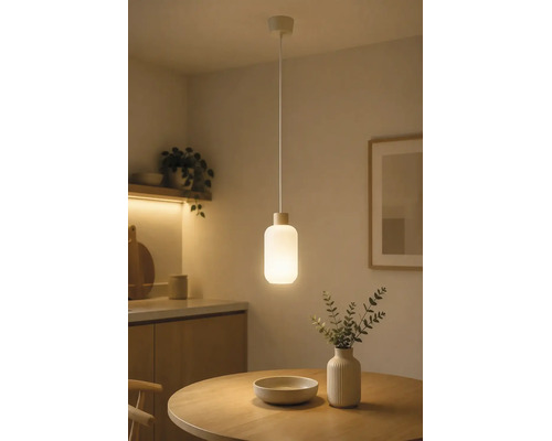 Moderne Pendelleuchte mit zylindrischem Glasschirm über einem runden Holztisch in einem minimalistisch eingerichteten Raum.