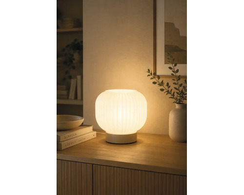 Beleuchtete Tischleuchte aus geriffeltem Glas auf einem Sideboard aus Holz, schafft eine warme Atmosphäre im Wohnbereich.