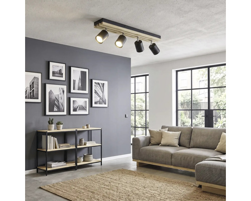 Vierflammiger Deckenstrahler aus Holz und Metall in einem modern eingerichteten Wohnzimmer mit Sofa und Regal.