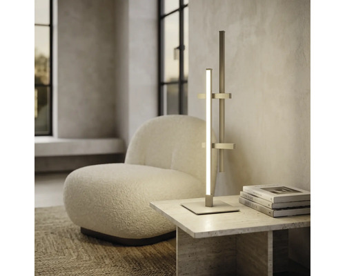Moderne LED-Tischleuchte im minimalistischen Design auf einem Steintisch neben einem weißen Bouclé-Sessel in einem hellen Wohnraum.
