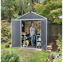 Frau steht in einem modernen Gartenhaus mit Doppeltür, Regalen, Wandaufbewahrung und Gartenwerkzeug in einem grünen Garten. (Image AI modified or generated)