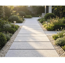 Moderner Gartenweg aus großformatigen, hellen Gehwegplatten, eingefasst von Kieselsteinen und üppiger Bepflanzung mit Wegeleuchten.