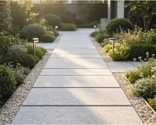 Moderner Gartenweg aus großformatigen, hellen Gehwegplatten, eingefasst von Kieselsteinen und üppiger Bepflanzung mit Wegeleuchten.