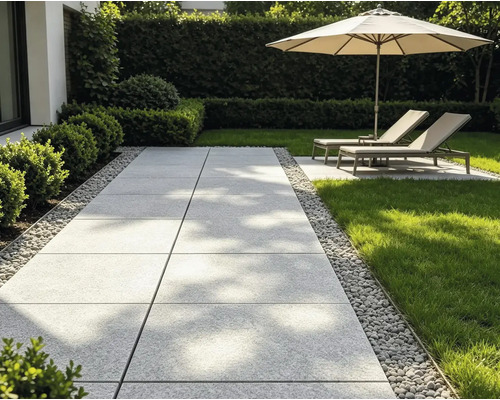 Moderner Gartenweg aus großen grauen Terrassenplatten mit Kiesumrandung, angrenzendem Rasen und Liegestühlen unter einem Sonnenschirm.