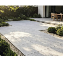 Moderne Gartenterrasse mit großformatigen Steinplatten, Kiesumrandung, Buchsbäumen und Gartenmöbeln im Hintergrund.