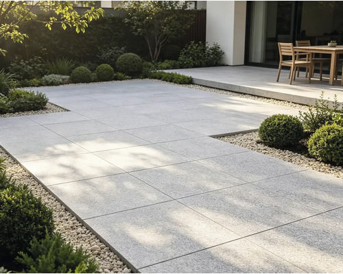 Moderne Gartenterrasse mit großformatigen Steinplatten, Kiesumrandung, Buchsbäumen und Gartenmöbeln im Hintergrund.