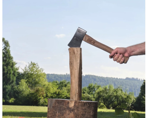 Eine Person spaltet mit einer For Q Spaltaxt einen Holzstamm auf einem Hackstock im Freien.