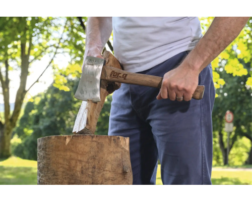 Eine Person spaltet mit einem for Q Spaltbeil Brennholz auf einem Baumstumpf im Freien.