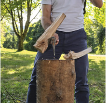 Ein Mensch spaltet einen Holzstamm im Freien mit einer Spaltaxt.