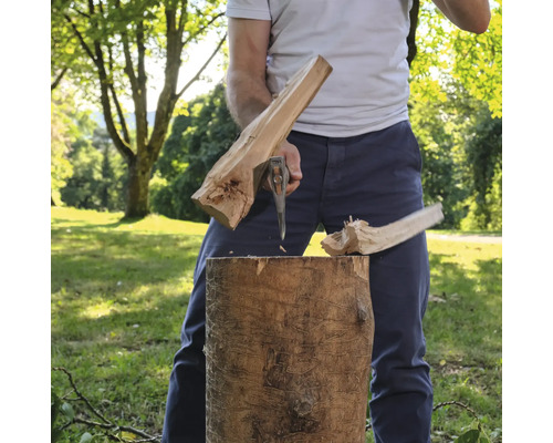 Ein Mensch spaltet einen Holzstamm im Freien mit einer Spaltaxt.