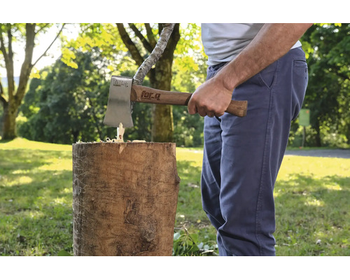 Eine Person benutzt eine For-Q Axt mit Holzstiel, um einen Holzstamm im Freien zu spalten.