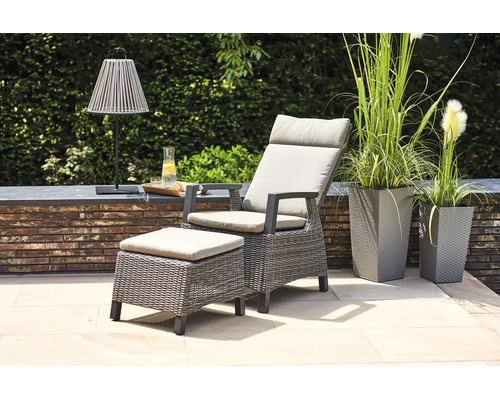 Gartensessel-Set aus Polyrattan mit Hocker und hellen Auflagen auf einer modernen Terrasse mit hohen Pflanzgefäßen.