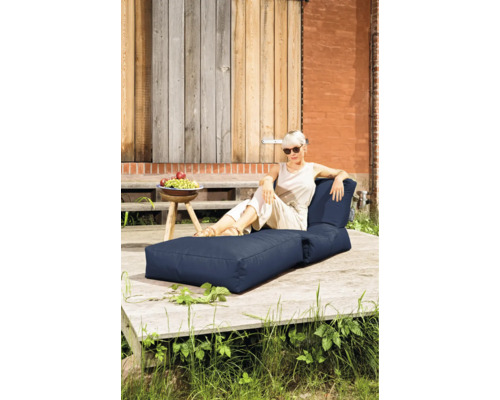 Eine Frau entspannt auf einem dunkelblauen, zweiteiligen Outdoor-Sitzsack-Lounge-Set auf einer hellen Holzterrasse.