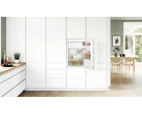 Einbaukühlschrank von Bosch mit offener Tür in einer modernen hellen Küche mit weißen Fronten und Holzfußboden.