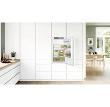 Einbaukühlschrank in einer modernen weißen Einbauküche mit offener Tür und Lebensmitteln in einem hellen, wohnlichen Ambiente.
